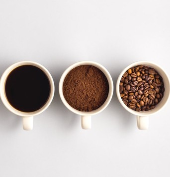 Trois mugs de café, dont un rempli de grains de cafés, l'autre de mouture de café, et le dernier d'un café liquide à boire