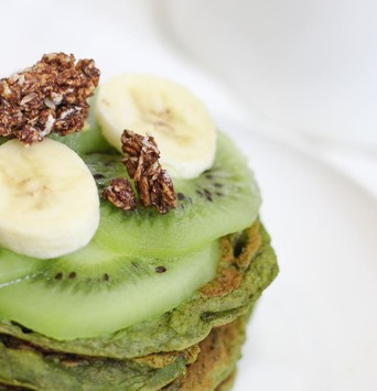 Pile de pancakes verts au matcha et à la banane, avec des tranches de banane et du granola en topping
