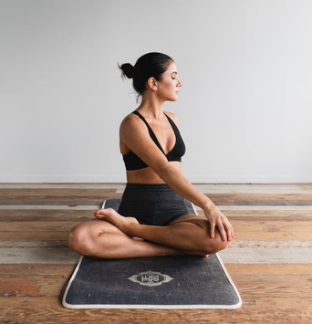 Jeune femme sur un tapis de yoga, assise en tailleur et faisant une torsion de la colonne vertébrale