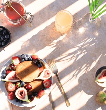 Assiette de pancakes avec des fruits frais et du miel comme exemple de quoi manger au petit-déjeuner