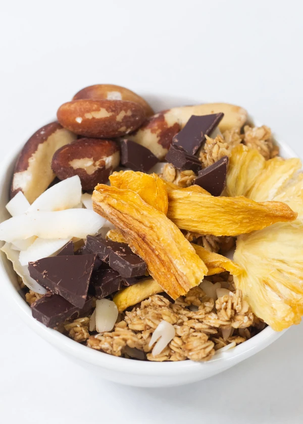 Bol avec granola, chocolat, copeaux de noix de coco, mangue séchée, graines de tournesol et ananas séché