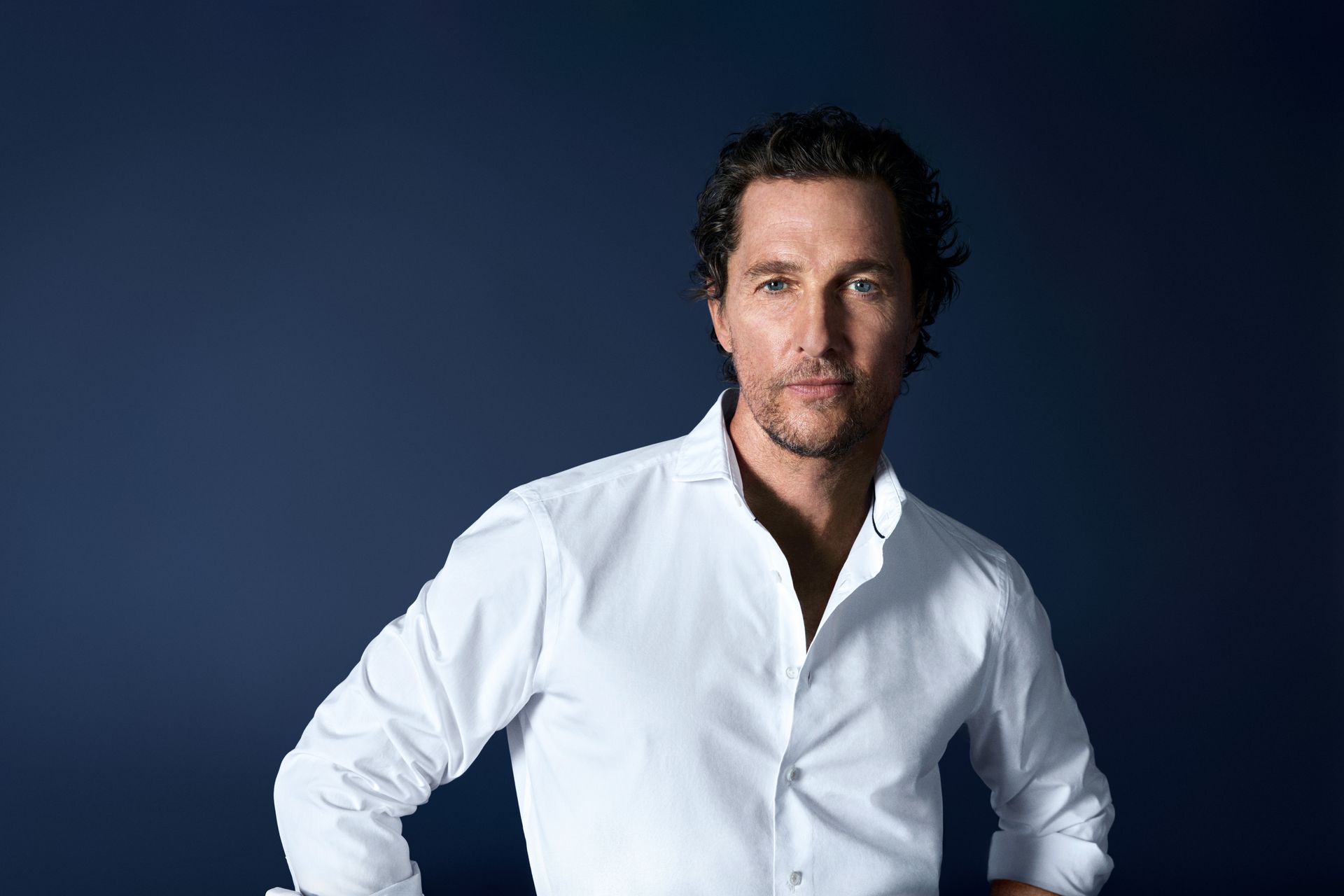 Matthew McConaughey trägt ein weißes OLYMP-Hemd vor dunklem Hintergrund.