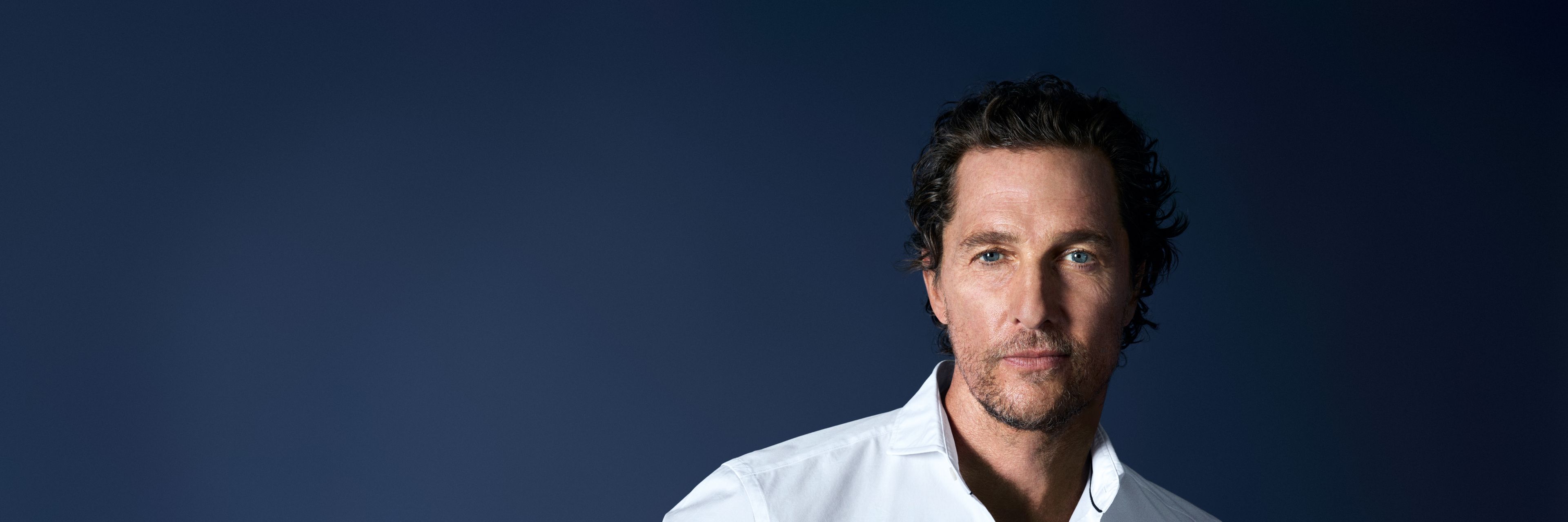 Matthew McConaughey trägt ein weißes OLYMP-Hemd vor dunklem Hintergrund.