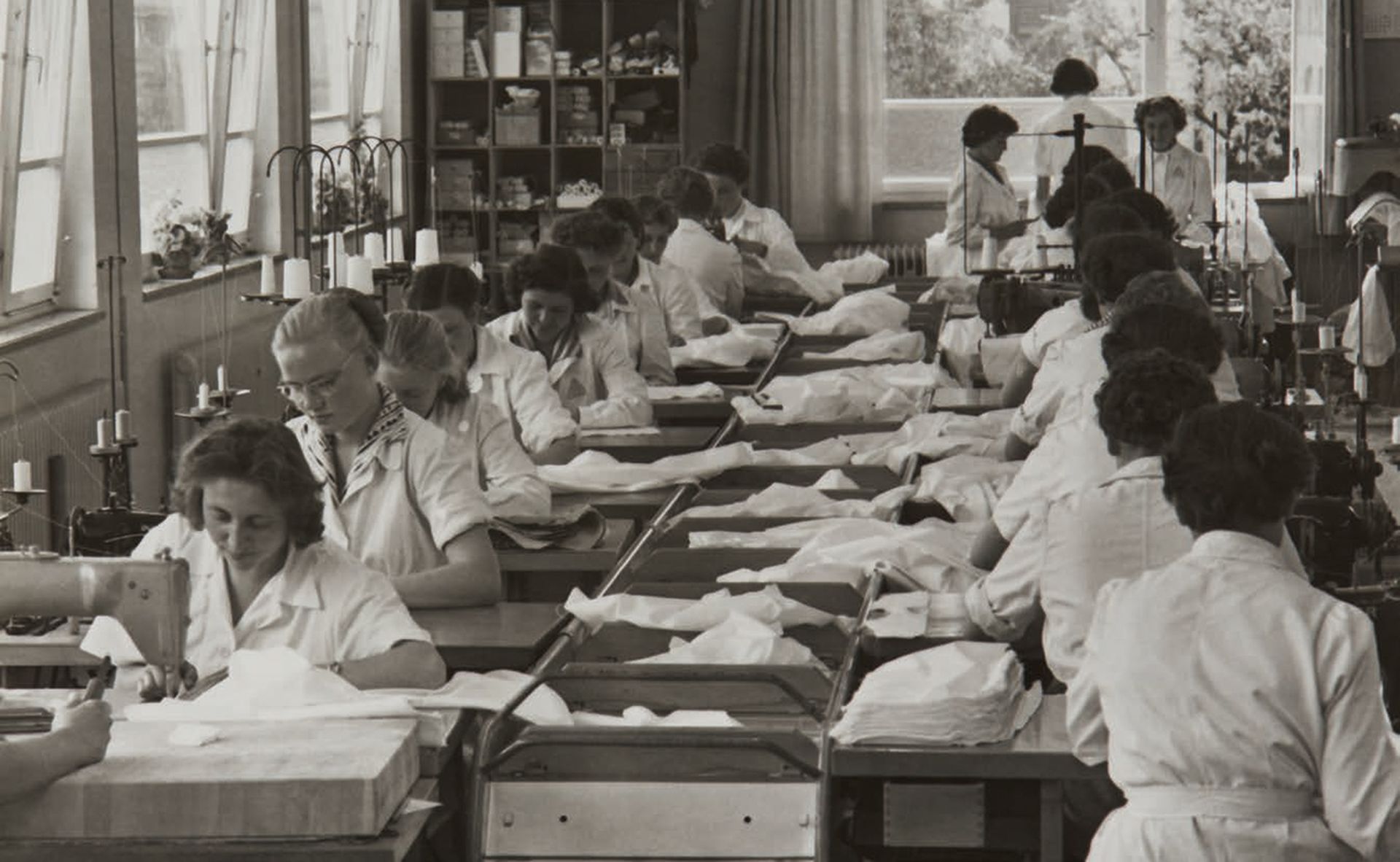 Historische Aufnahme der OLYMP Produktion in den 1960er Jahren mit mehreren Mitarbeitern beim Nähen von Hemden an Nähmaschinen.