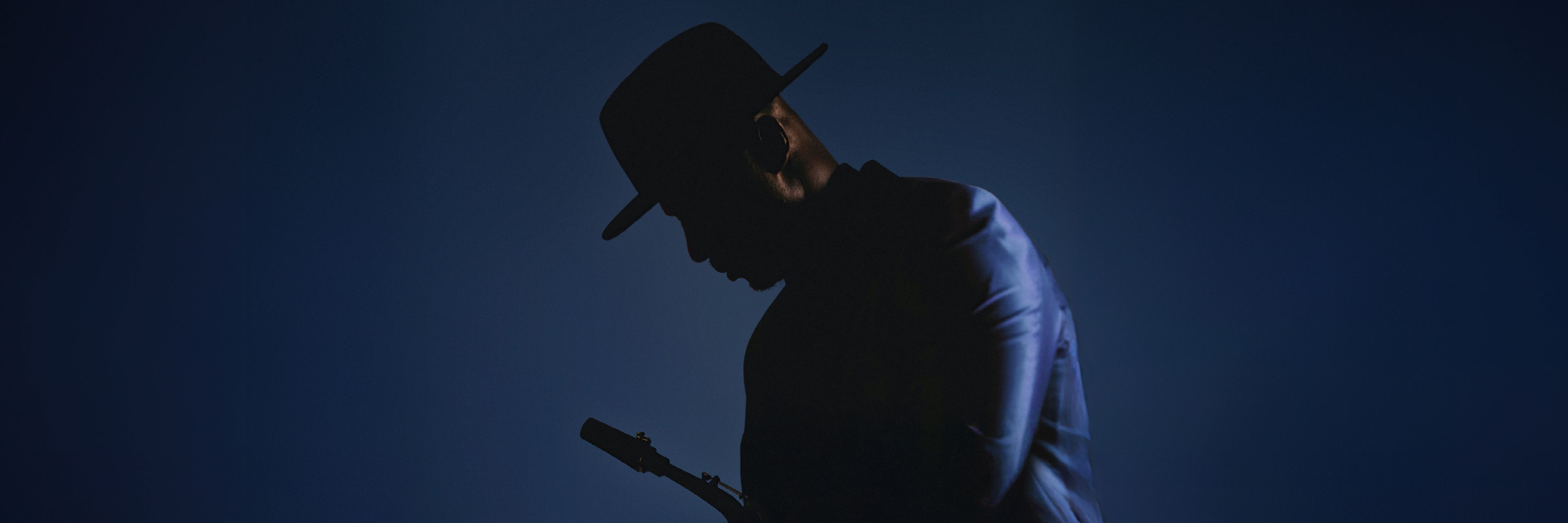 Silhouette eines Jazzmusikers mit Hut und Anzug, der ein Saxophon hält, vor blauem Hintergrund.