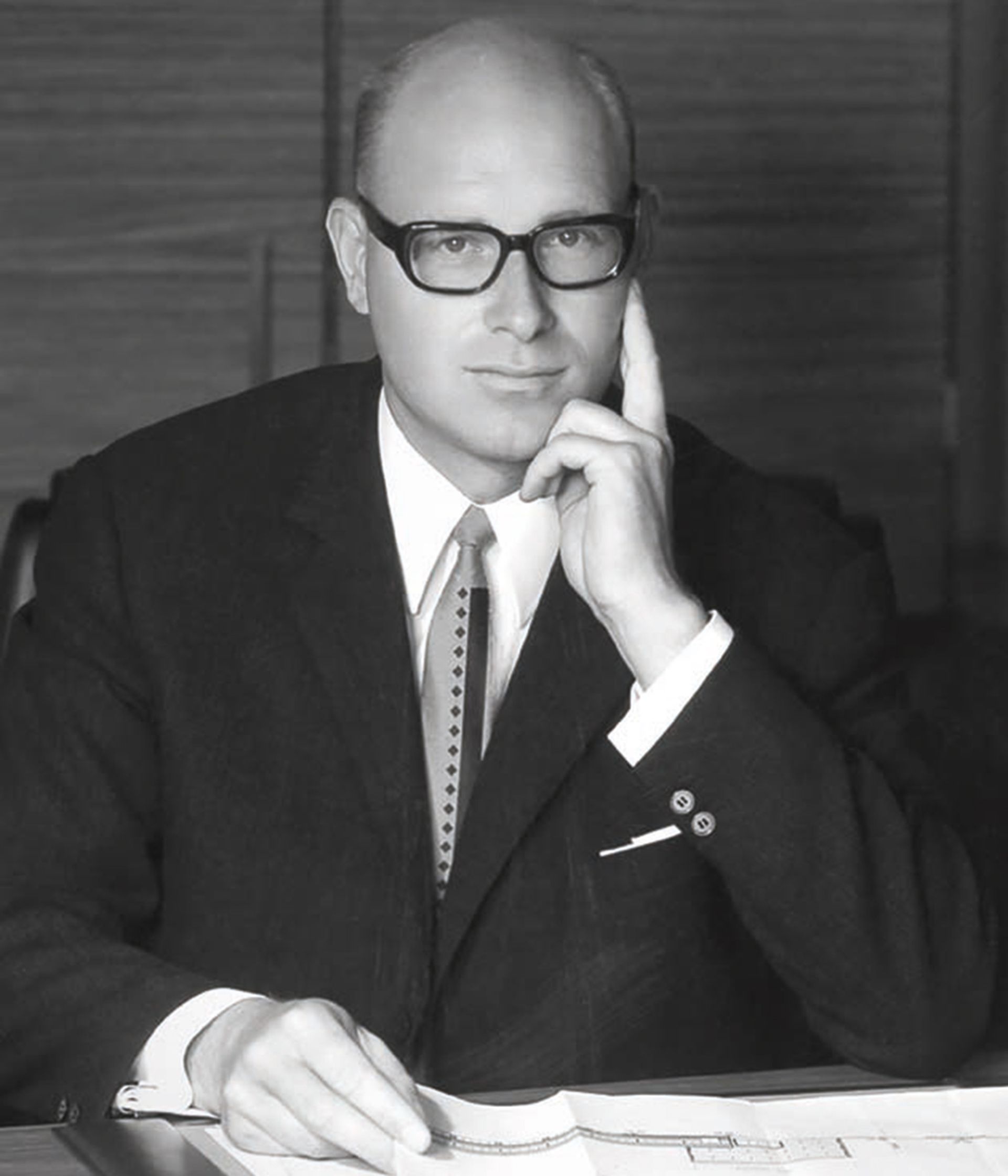 Schwarz-weißes Porträt von Eberhard Bezner im Anzug mit Krawatte und Brille, sitzend am Schreibtisch.