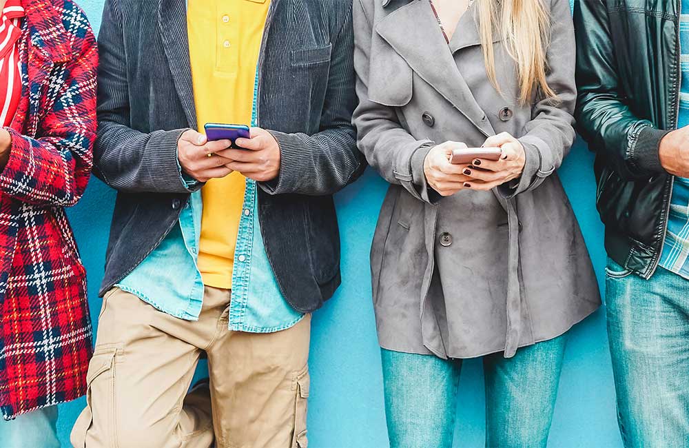 Vier Personen stehen vor einer blauen Wand, jede hält ein Smartphone in der Hand und ist leger und stilvoll gekleidet.