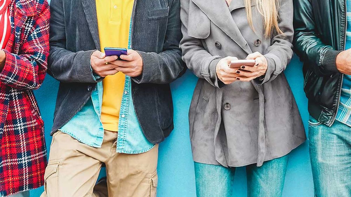 Vier Personen stehen vor einer blauen Wand, jede hält ein Smartphone in der Hand und ist leger und stilvoll gekleidet.
