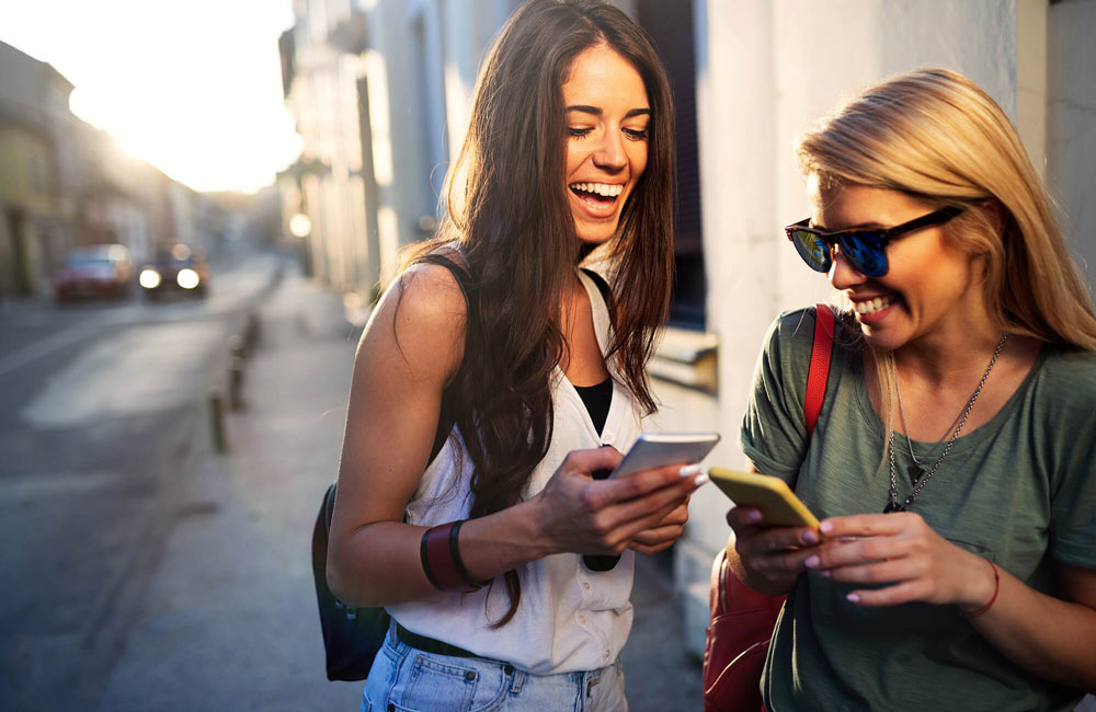Zwei junge Frauen unterhalten sich und benutzen ihre Smartphones.
