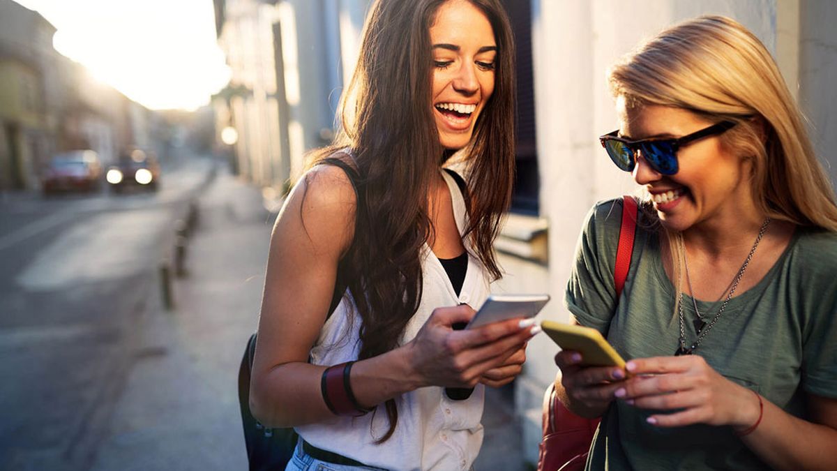 Zwei junge Frauen unterhalten sich und benutzen ihre Smartphones.