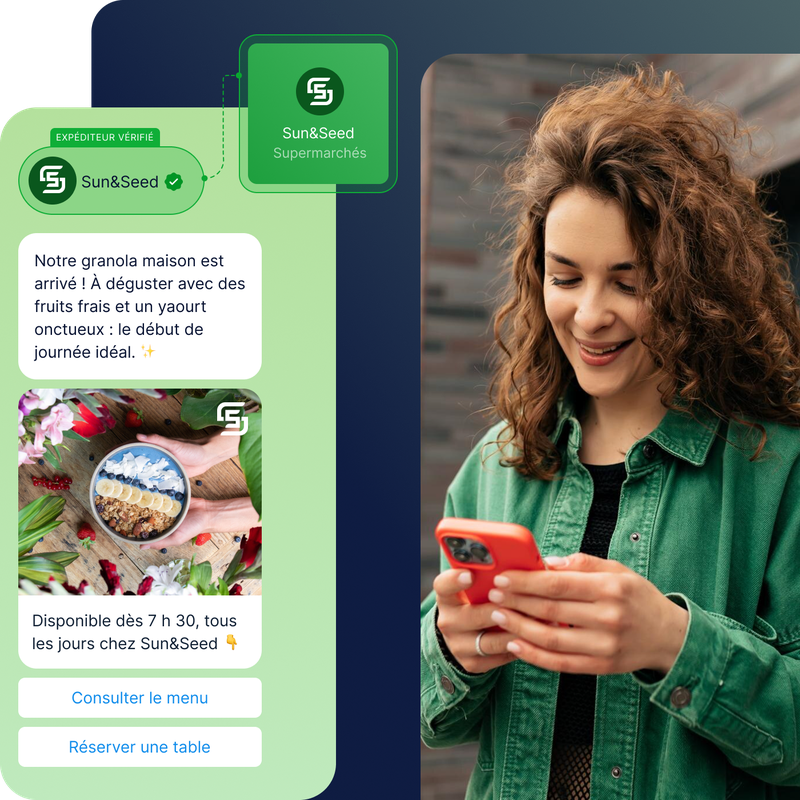 Une femme souriante aux cheveux bouclés lit sur son téléphone un message concernant le nouveau granola maison de Sun&Seed, disponible tous les jours, accompagné d'une photo d'un bol garni de fruits.