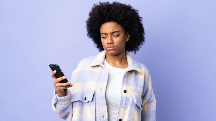 Eine Person blickt mit missmutiger Miene auf ihr Handy.