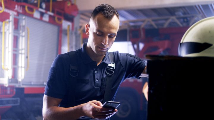 Ein Feuerwehrmann in einer Feuerwache schaut auf ein Mobiltelefon.