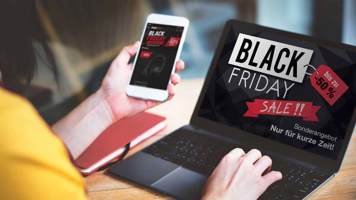Eine Person, die ein Smartphone und einen Laptop auf dessen Bildschirm ist eine Black-Friday-Werbeanzeige mit bis zu 50 % Rabatt zu sehen.