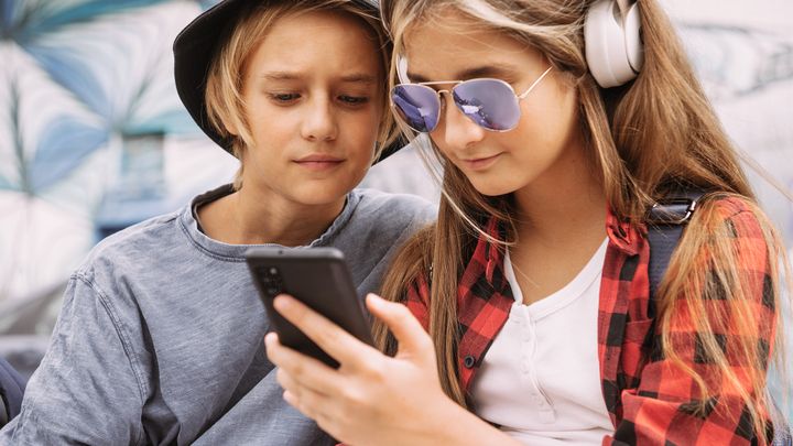 Zwei Kinder der Generation Alpha sehen zusammen auf ein Handy.