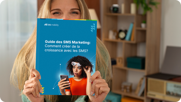 Une personne tenant un livre intitulé « Guide des SMS Marketing : Comment créer de la croissance avec les SMS ? », dont la couverture représente une femme surprise, dans une pièce chaleureuse.