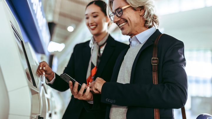 Mann beim Check-in am Flughafen. Einchecken von Handgepäck wird über mobile Kanäle wie SMS und WhatsApp besonders einfach.