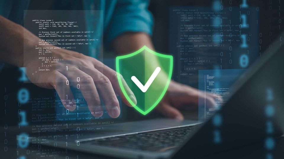 Hände an einem Laptop mit Programmiercode, darüber ein leuchtendes Schutzschild mit Häkchen als Symbol für sichere Daten und geschützte IT-Systeme.