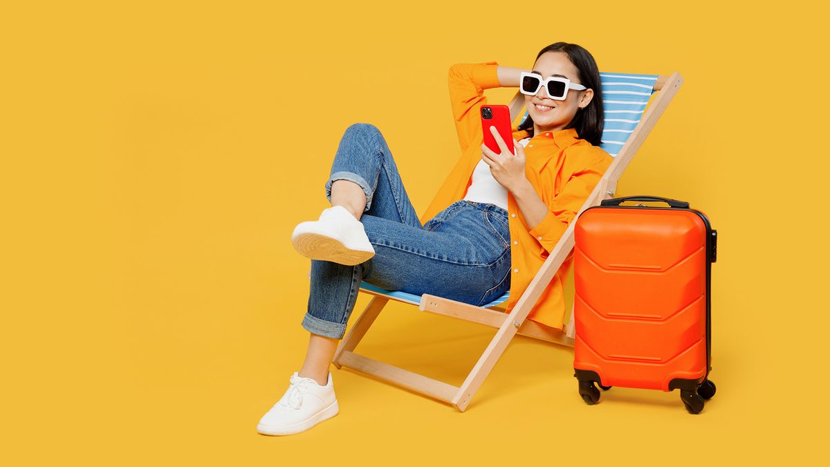 Eine Frau mit Sonnenbrille, die auf einem Liegestuhl entspannt und ihr Smartphone benutzt, neben ihr steht ein orangefarbener Koffer, vor einem gelben Hintergrund.