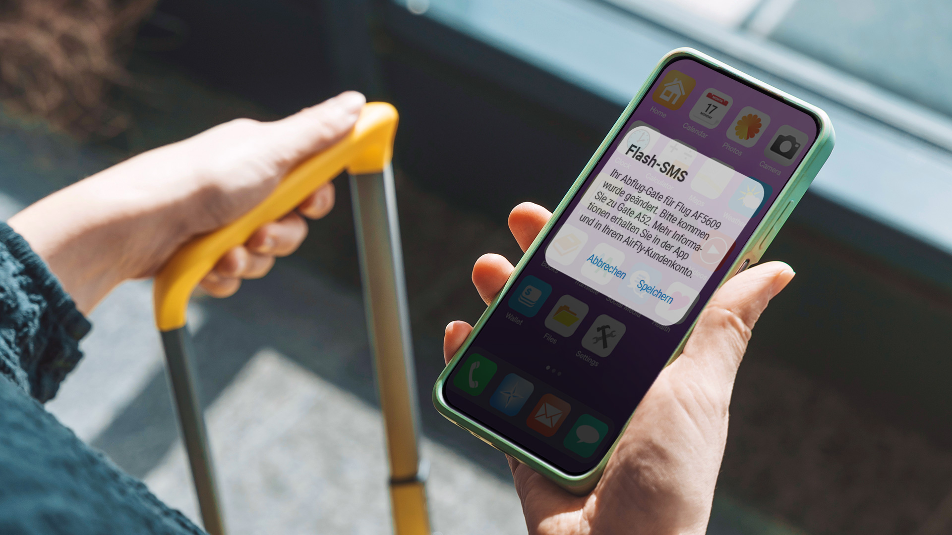 Eine Person hält einen Koffergriff und ein Smartphone auf dessen Bildschirm eine Flash-SMS angezeigt wird.
