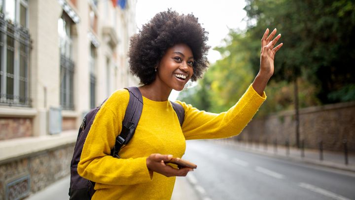 Eine junge Frau winkt dem Flughafen-Taxi, dass sie per SMS gebucht hat.