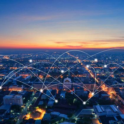 Stadtansicht bei Sonnenuntergang mit zahlreichen miteinander verbundenen Datenpunkten und Netzwerkverbindungen als Symbol für digitale Vernetzung und sichere Datenübertragung.“