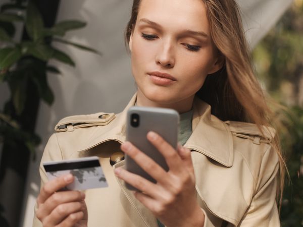 Woman using smartphone and credit card, illustrating secure mobile transactions and customer engagement as described in the SMS Marketing Guide.