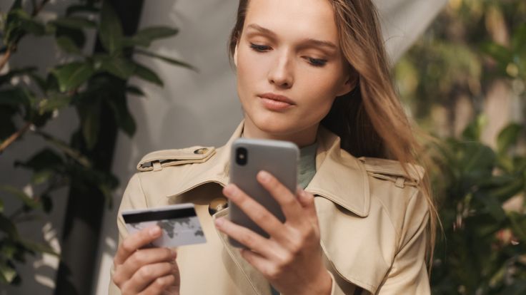 Woman using smartphone and credit card, illustrating secure mobile transactions and customer engagement as described in the SMS Marketing Guide.