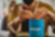 Zwei Hände werfen Kleingeld in eine blaue Spendendose mit dem clubkinder Logo drauf.