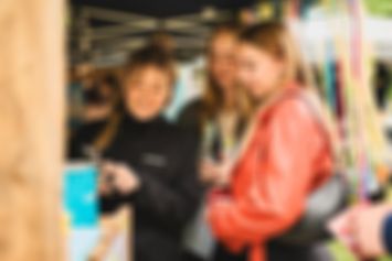 Drei Personen stehen an einem bunten Stand. Sie schauen auf ein Handy und lächeln.