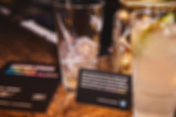 Gläser mit Getränken auf einem Tresen. Daneben steht eine Visitenkarte mit Infos zum Spendenclub Unterm Strich.