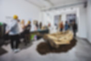 Mehrere Personen in einer Galerie. In der Mitte steht ein Holzschiff. Daneben und dahinter wird sich unterhalten.
