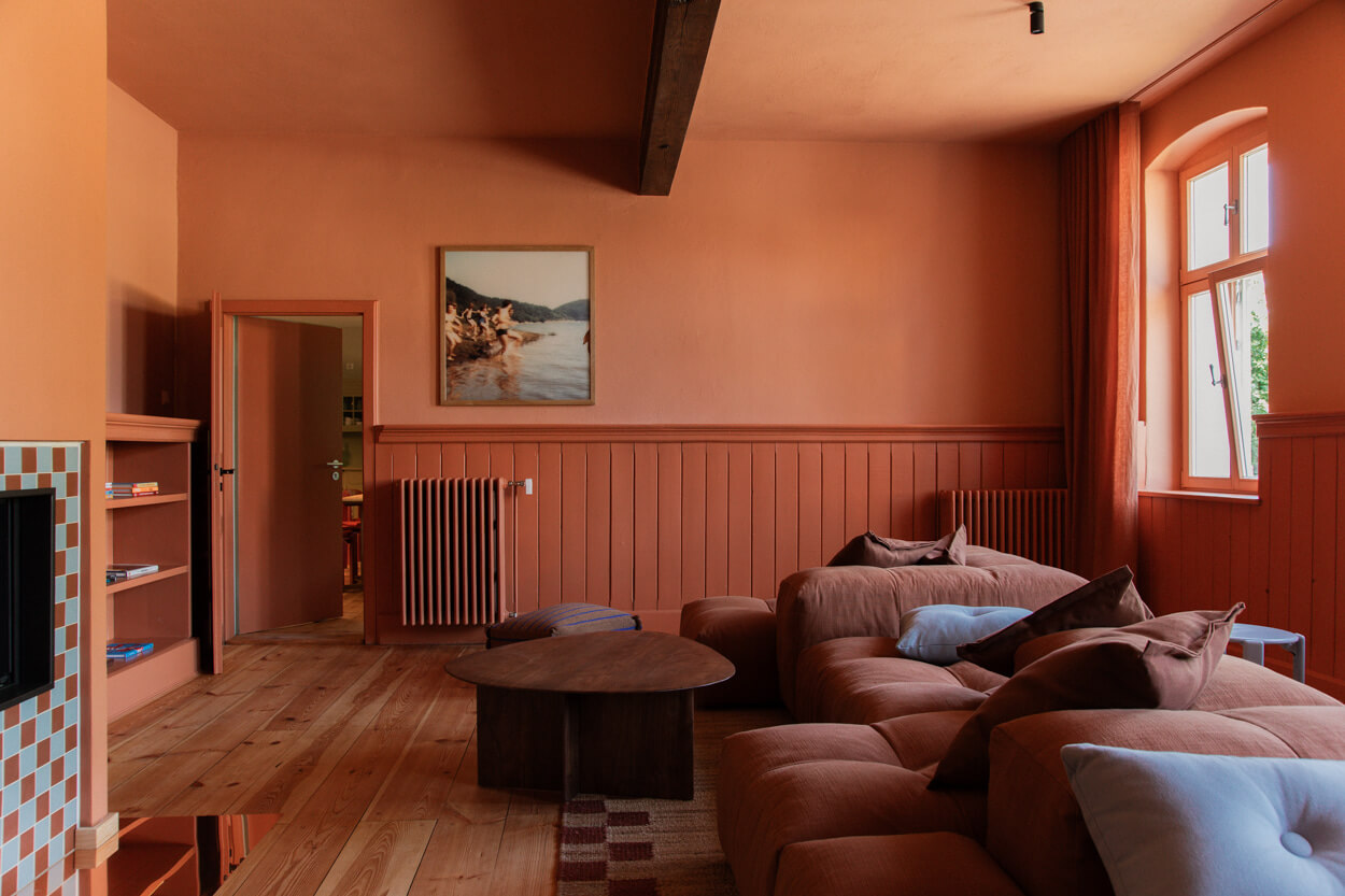 Cozy living room with terracotta walls, a large brown sectional sofa, wooden floors, a round coffee table, and a framed landscape photo.
