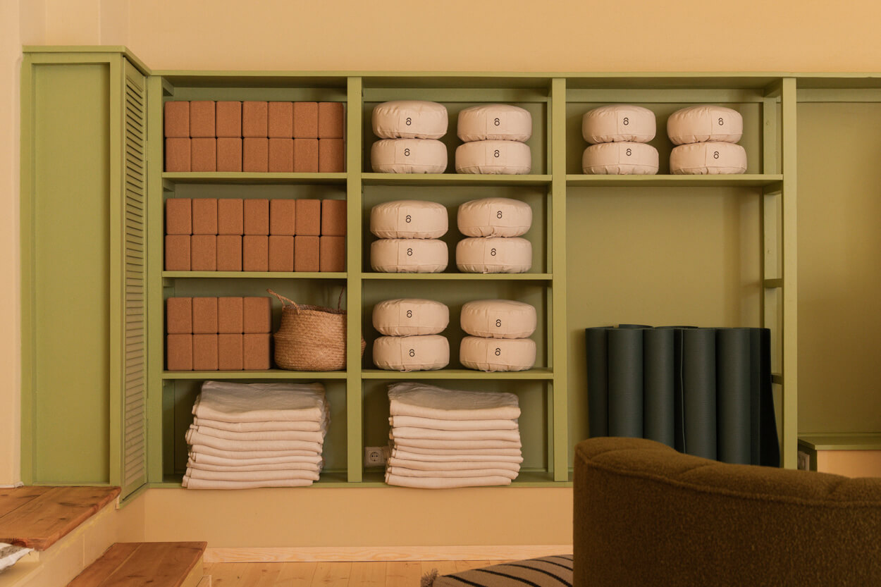Shelves with neatly stacked yoga mats, towels, bolsters, and boxes in a calming, organized space with green accents.