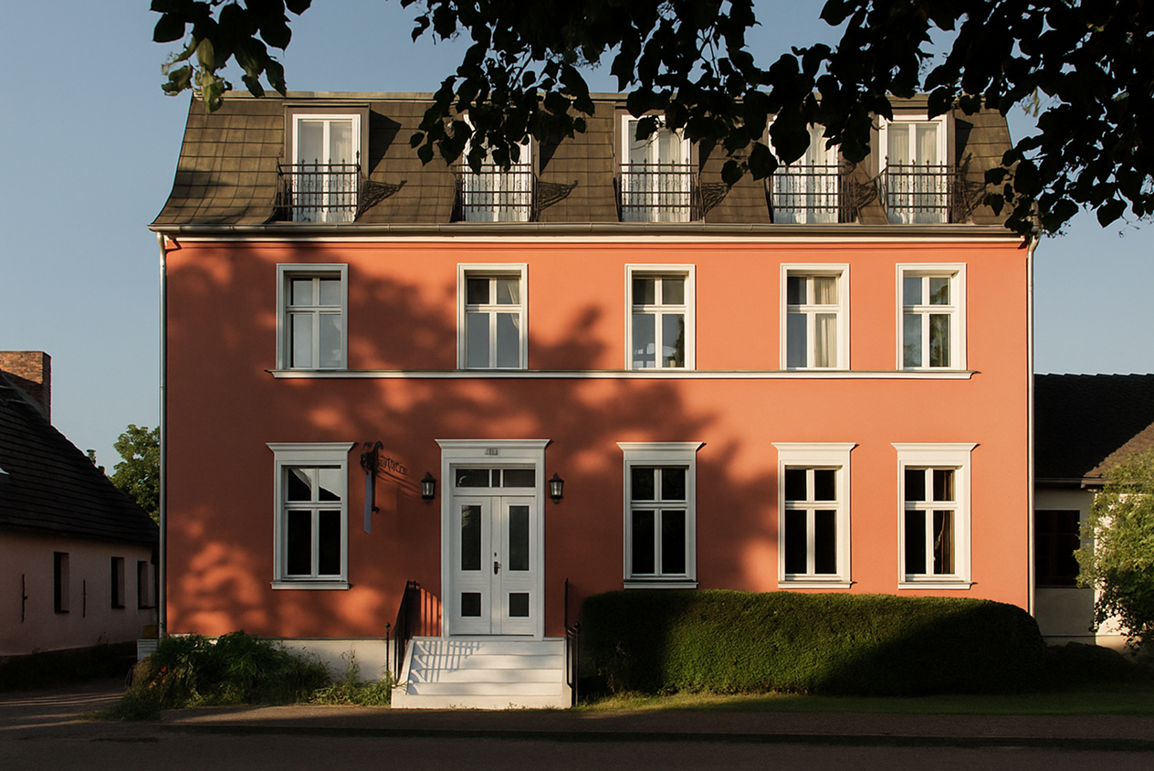 A peach-colored, three-story house with white-framed windows and a white door, surrounded by greenery, under a clear sky.