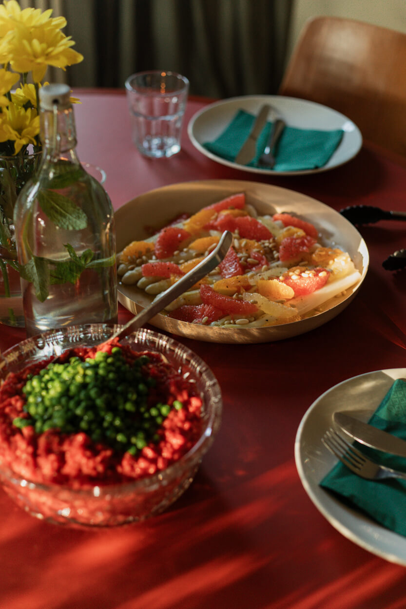 Table set with a plate of grapefruit and citrus salad, a bowl of beet and pea salad, a water bottle, yellow flowers, and neatly arranged plates.