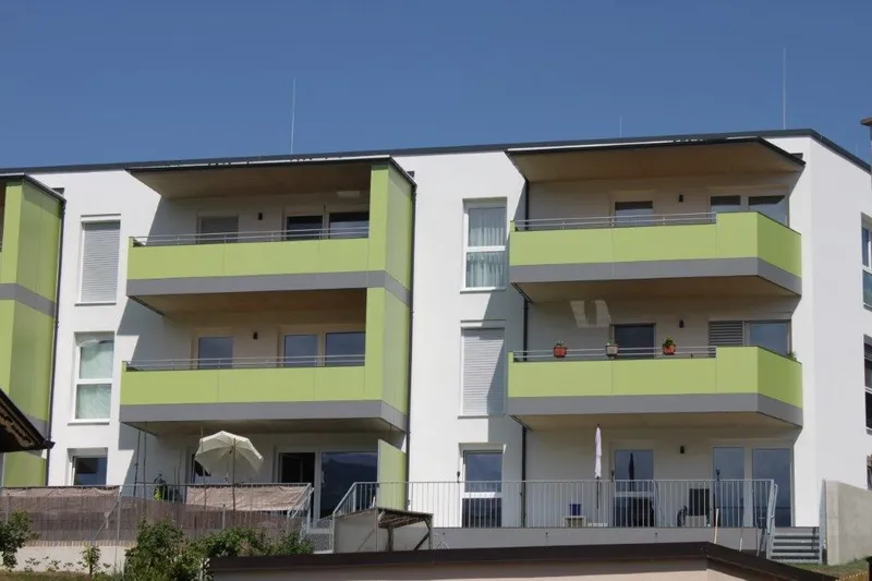 A modern apartment building with green balconies and large windows under a clear blue sky.