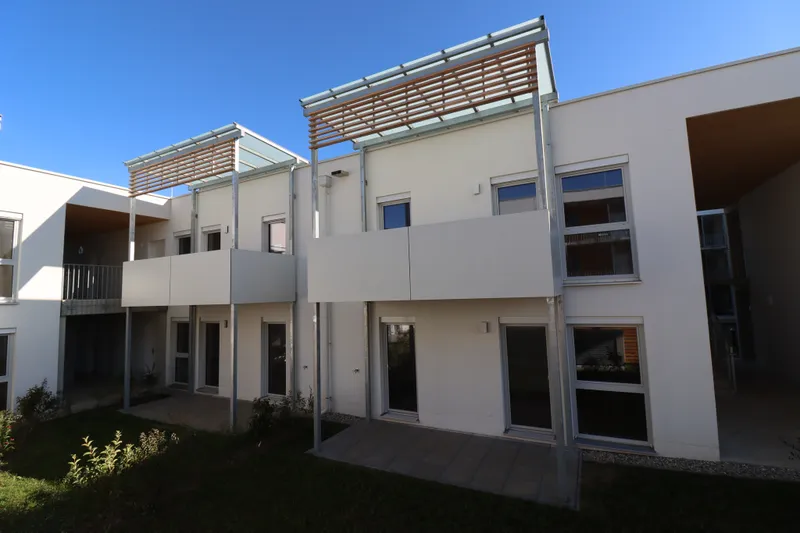 Modern white apartment building with balconies, large windows, and metal pergolas under a clear blue sky.