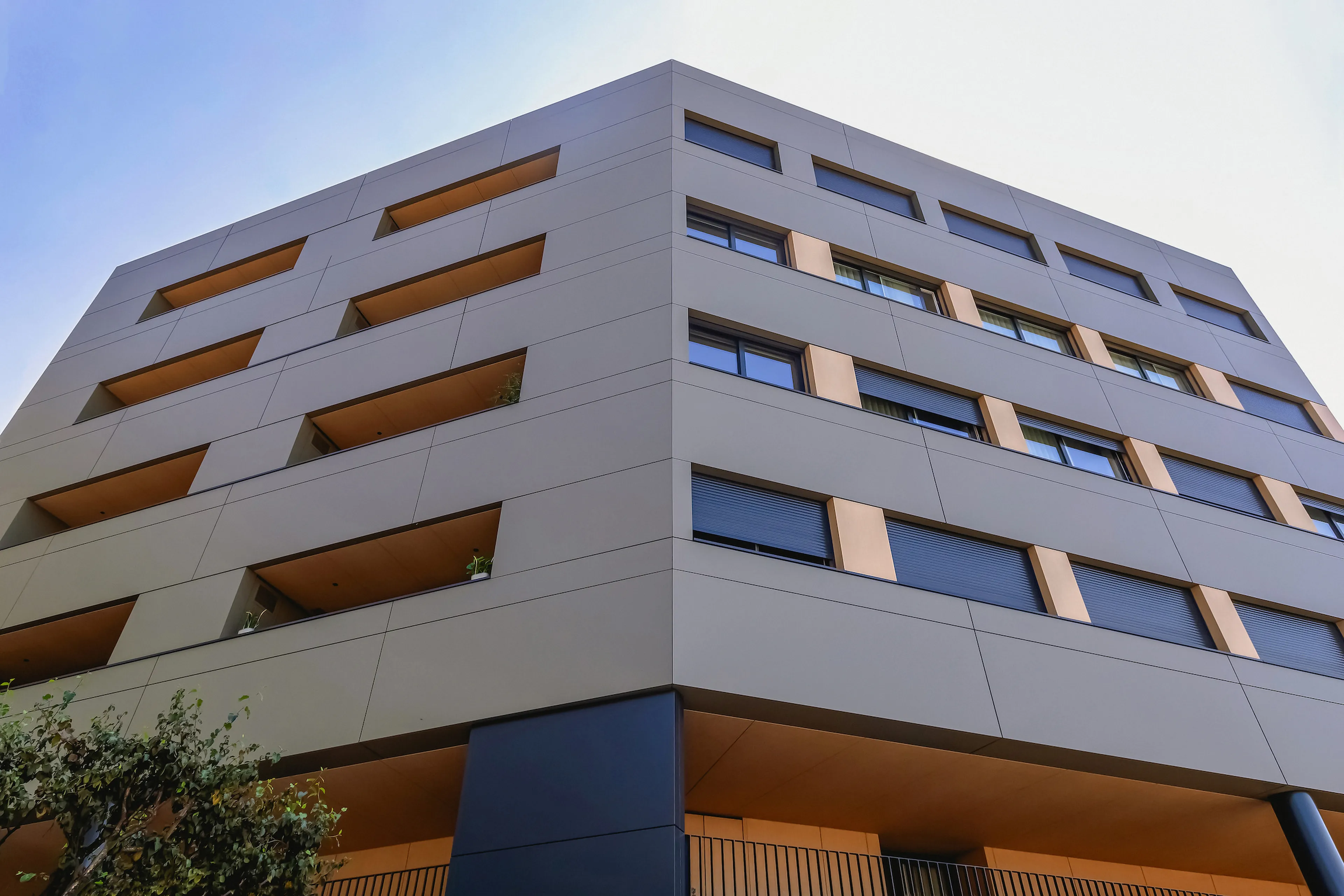 Modern six-story building with a geometric facade, featuring windows and balconies, under a clear blue sky.