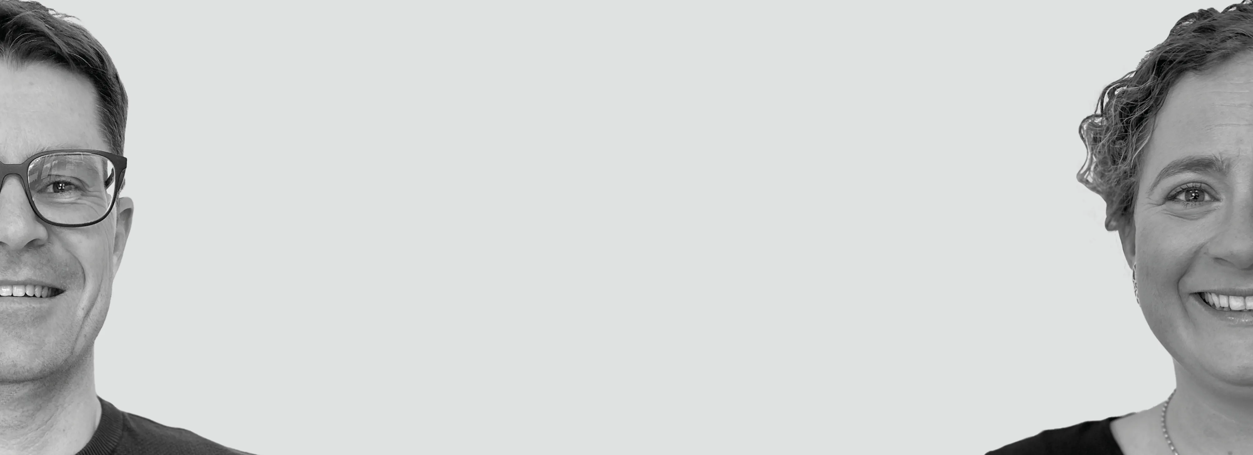 Black and white image of two people smiling, each partially visible on the left and right edges against a plain background.