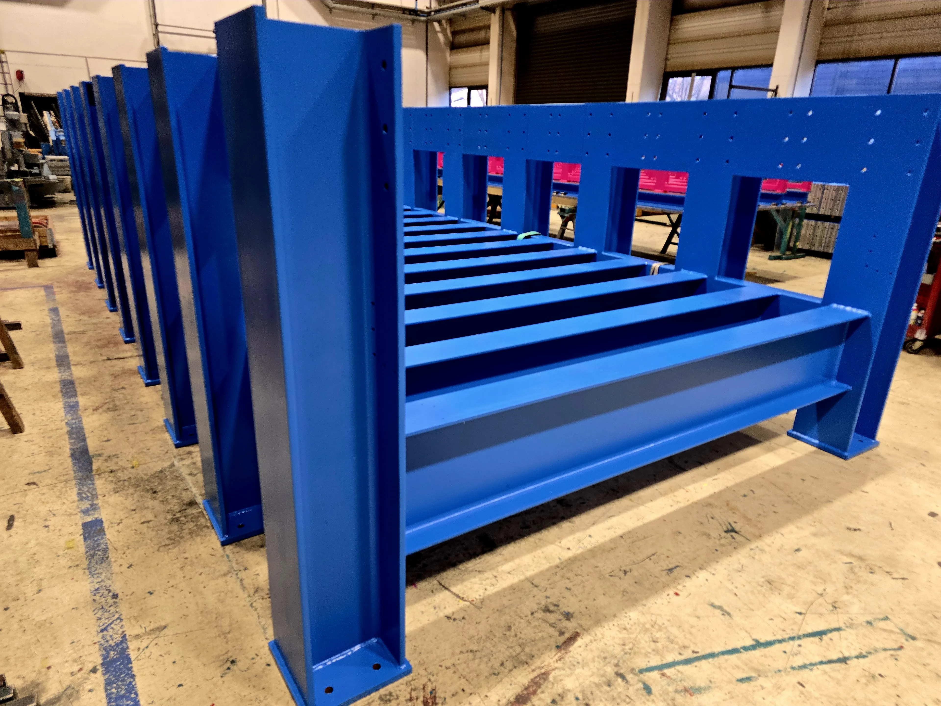 Detailansicht von einem großen blauen Stahlgestell mit mehreren Balken, aufgestellt in der Werkstatt von SENO Spezialmaschinen.