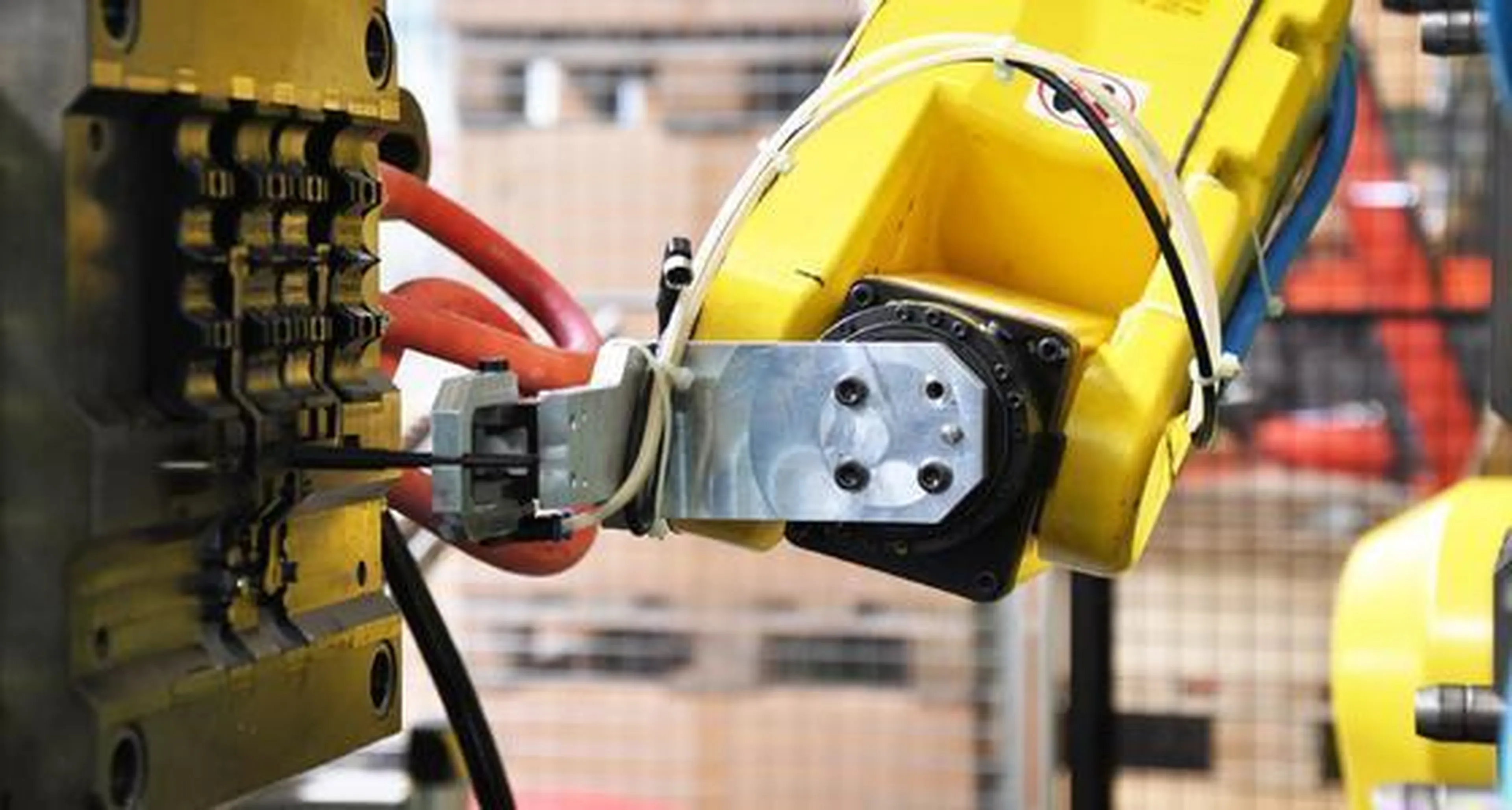 A yellow robotic arm operates machinery in an industrial setting, gripping a tool near a metal component with wires attached. Picture for Manufacturing