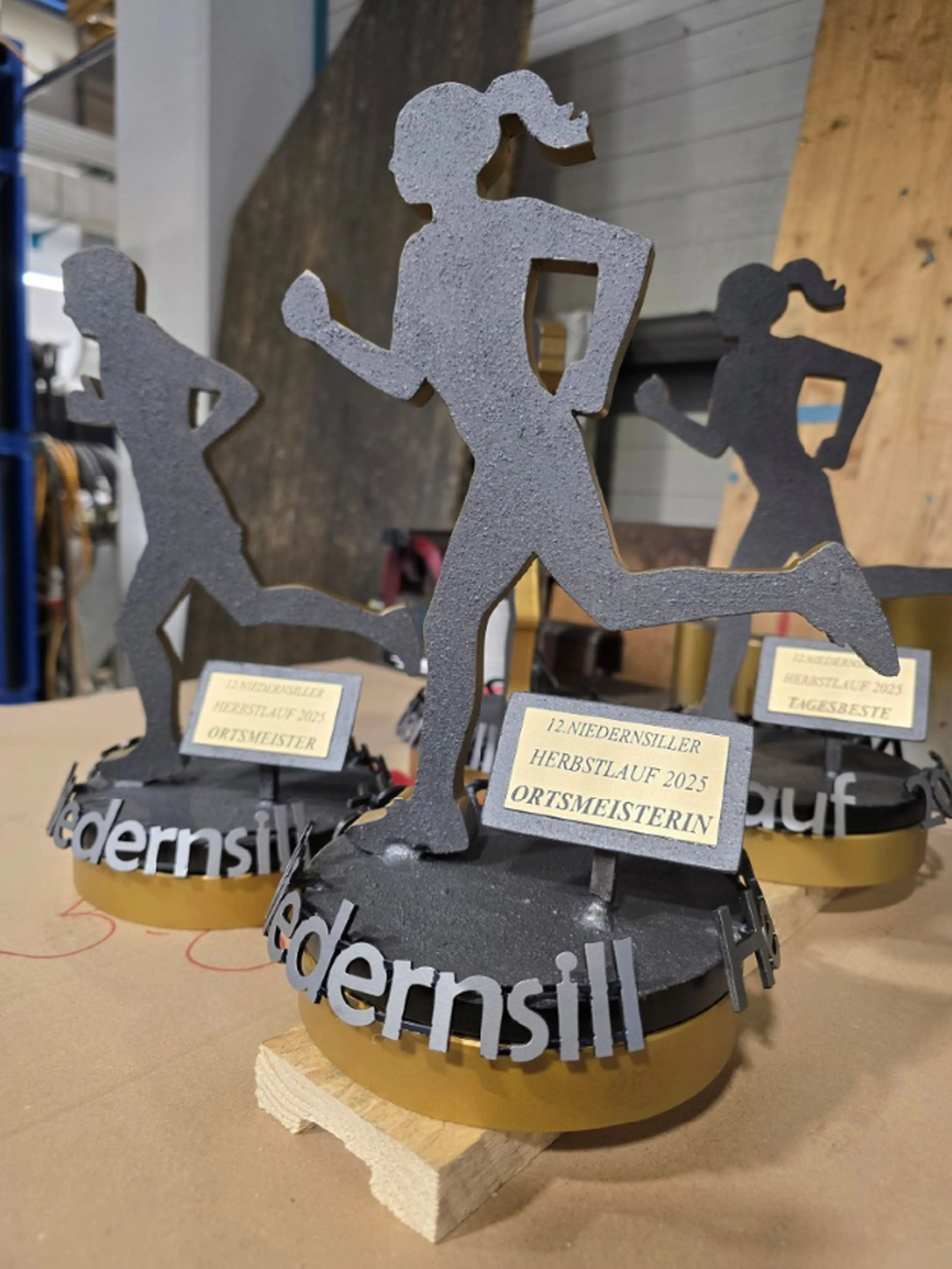 Fertige Pokale für den Niedernsiller Herbstlauf 2025; 1 männlicher und 2 weibliche Läufer aus Stahl, mit Farbe lackiert, auf einem runden, drehbaren Stahlsockel mit dem gelaserten Schild "Ortsmeisterin bzw. Ortsmeister"