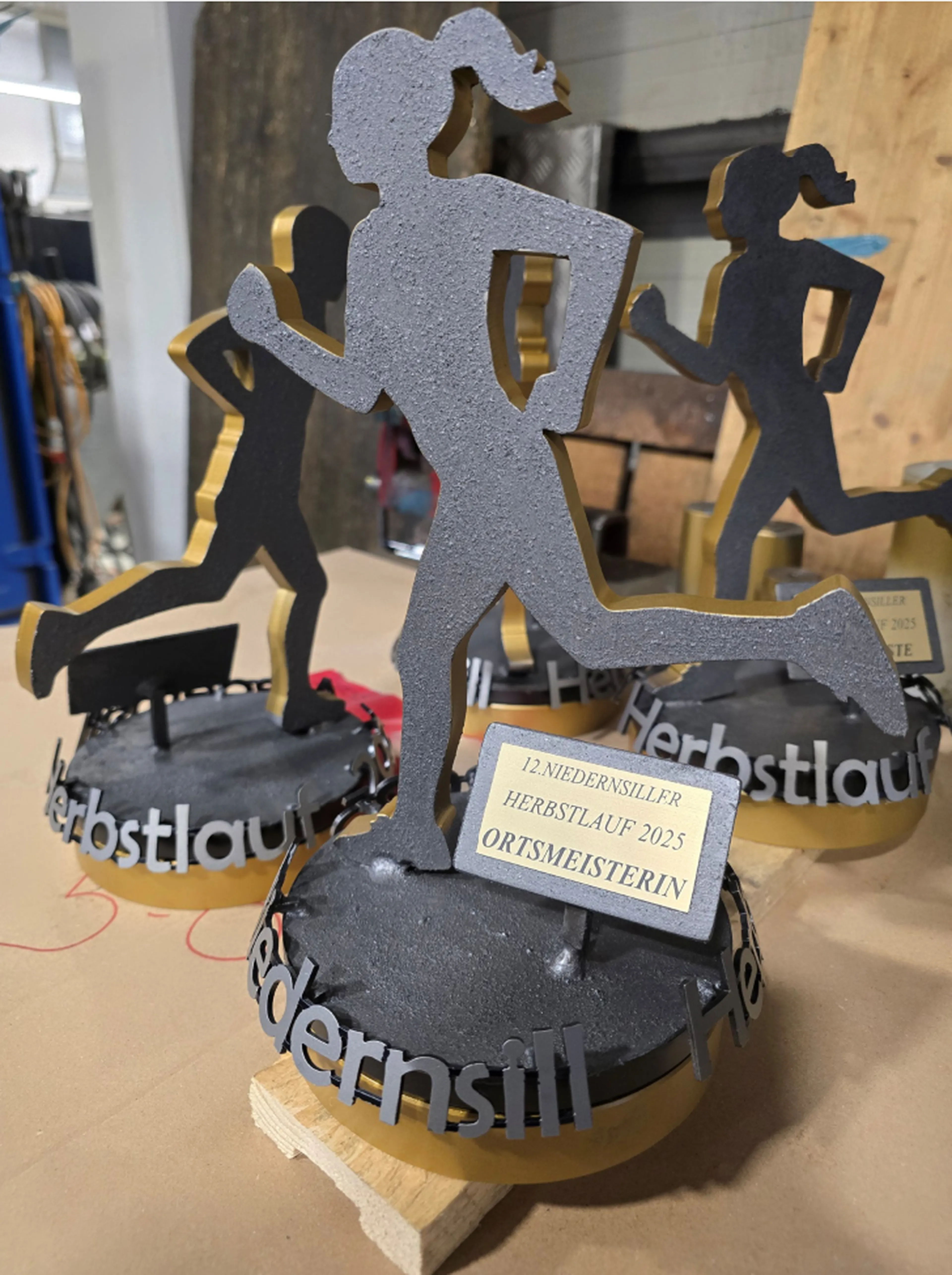 Fertige Pokale für den Niedernsiller Herbstlauf 2025; 1 männlicher und 2 weibliche Läufer aus Stahl, mit Farbe lackiert, auf einem runden, drehbaren Stahlsockel mit dem gelaserten Schild "Ortsmeisterin bzw. Ortsmeister"