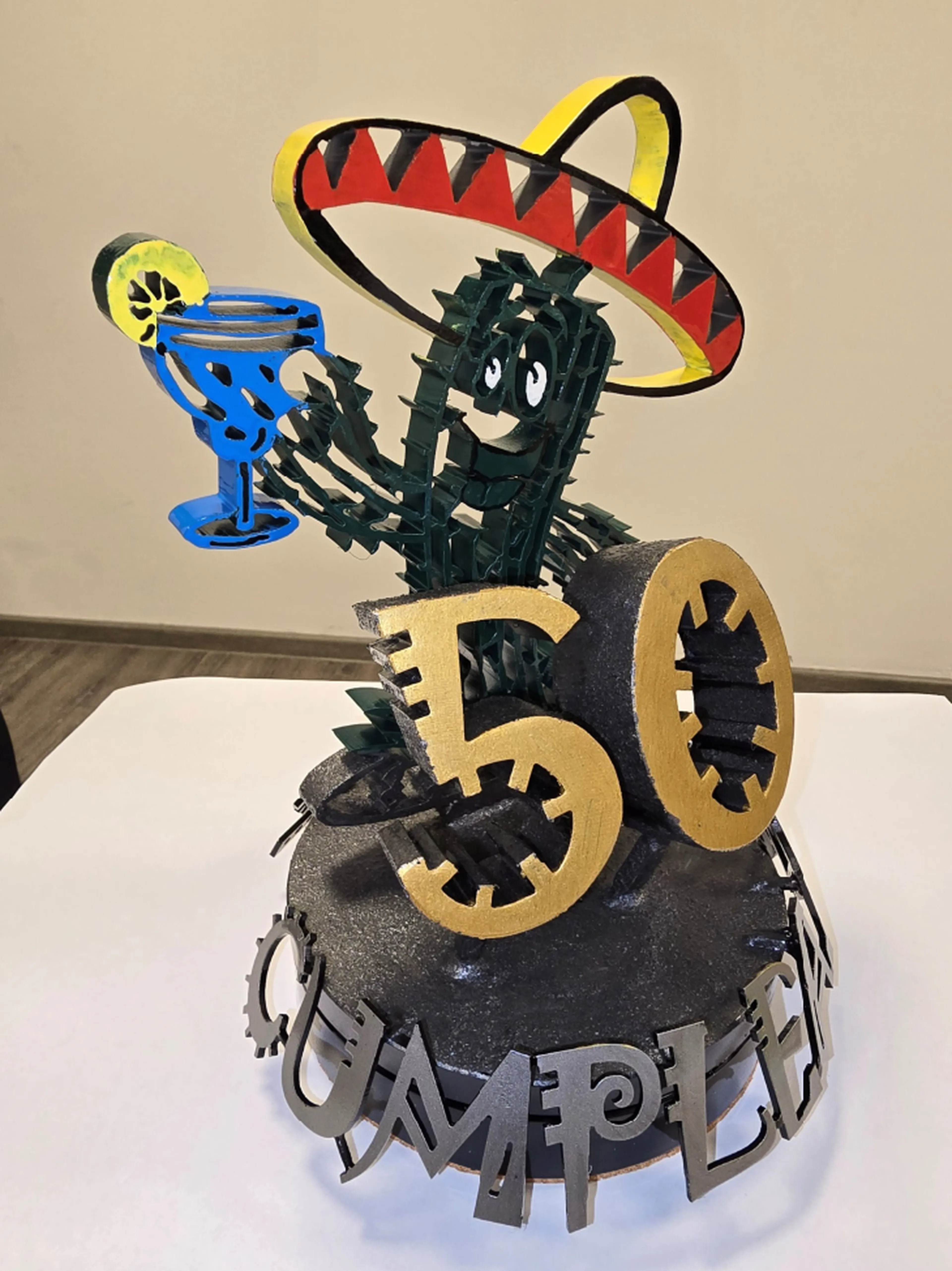 Fröhlicher Kaktus mit Sombrero, einem Drink in der Hand, einer großen „50” und dem Wort „CUMPLEAÑOS” auf einem dekorativen, drehbaren Sockel.