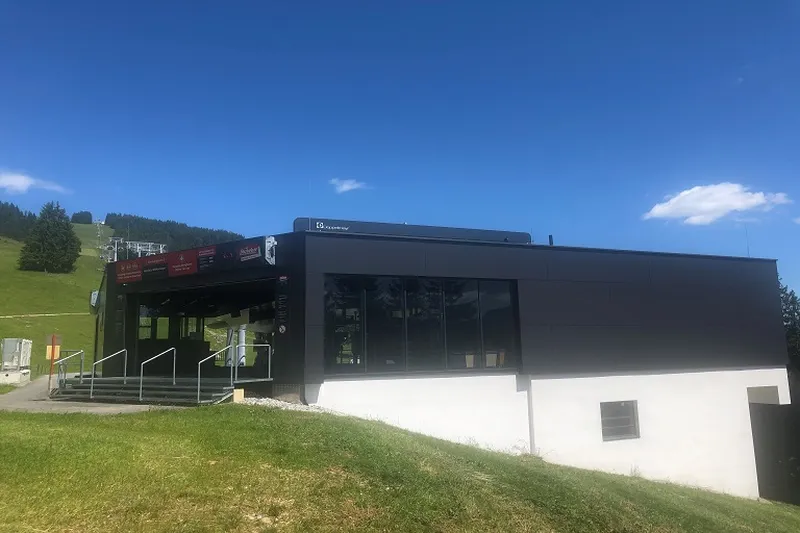 Modern building with dark exterior, large windows, and a sloped grassy hill beside. Clear blue sky in the background.