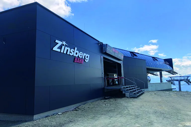 Zinsberg Bahn station building with modern design, located at a mountainside, under a clear blue sky.