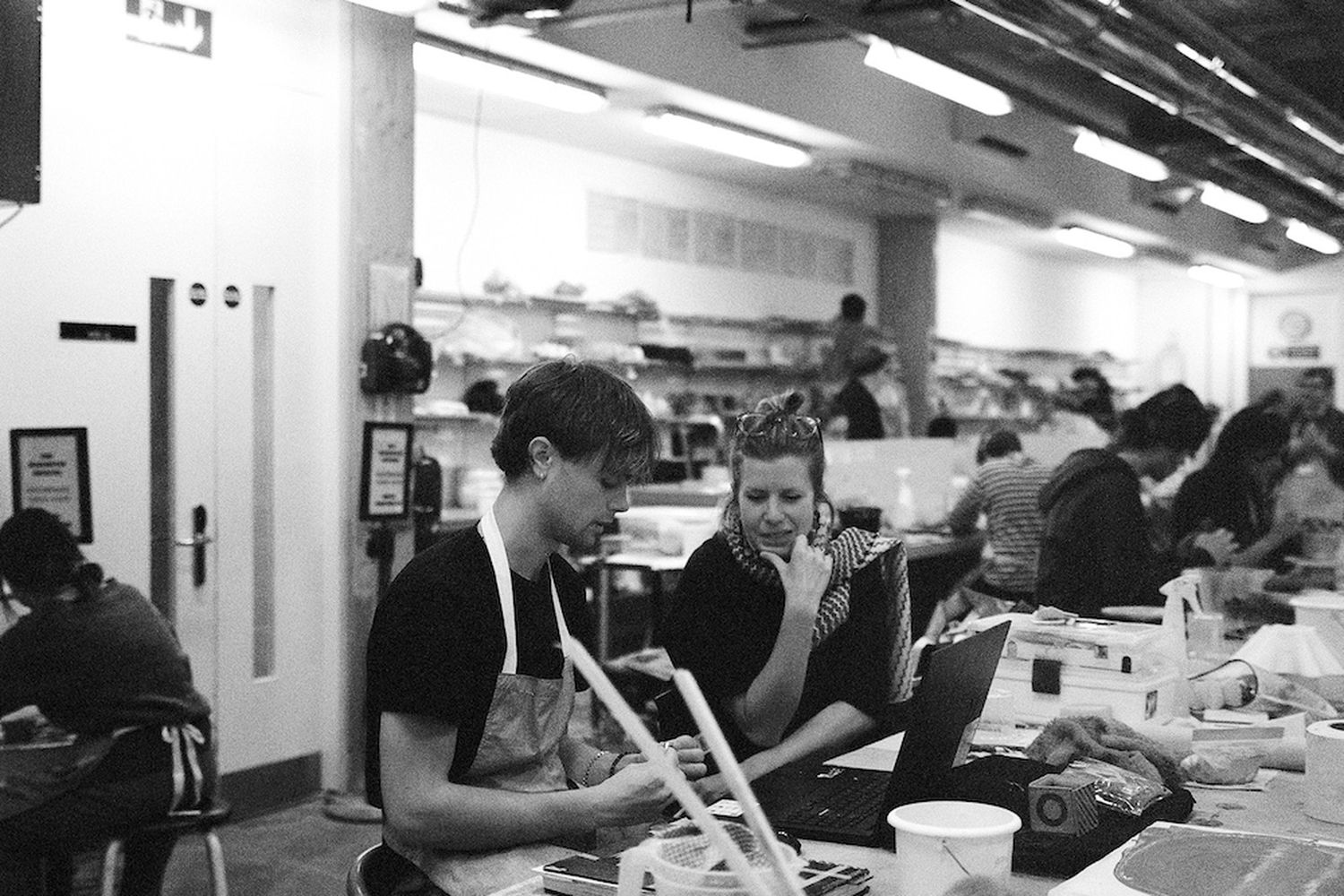 A black and white photograph of a male and female artist discussing and preparing their projects.