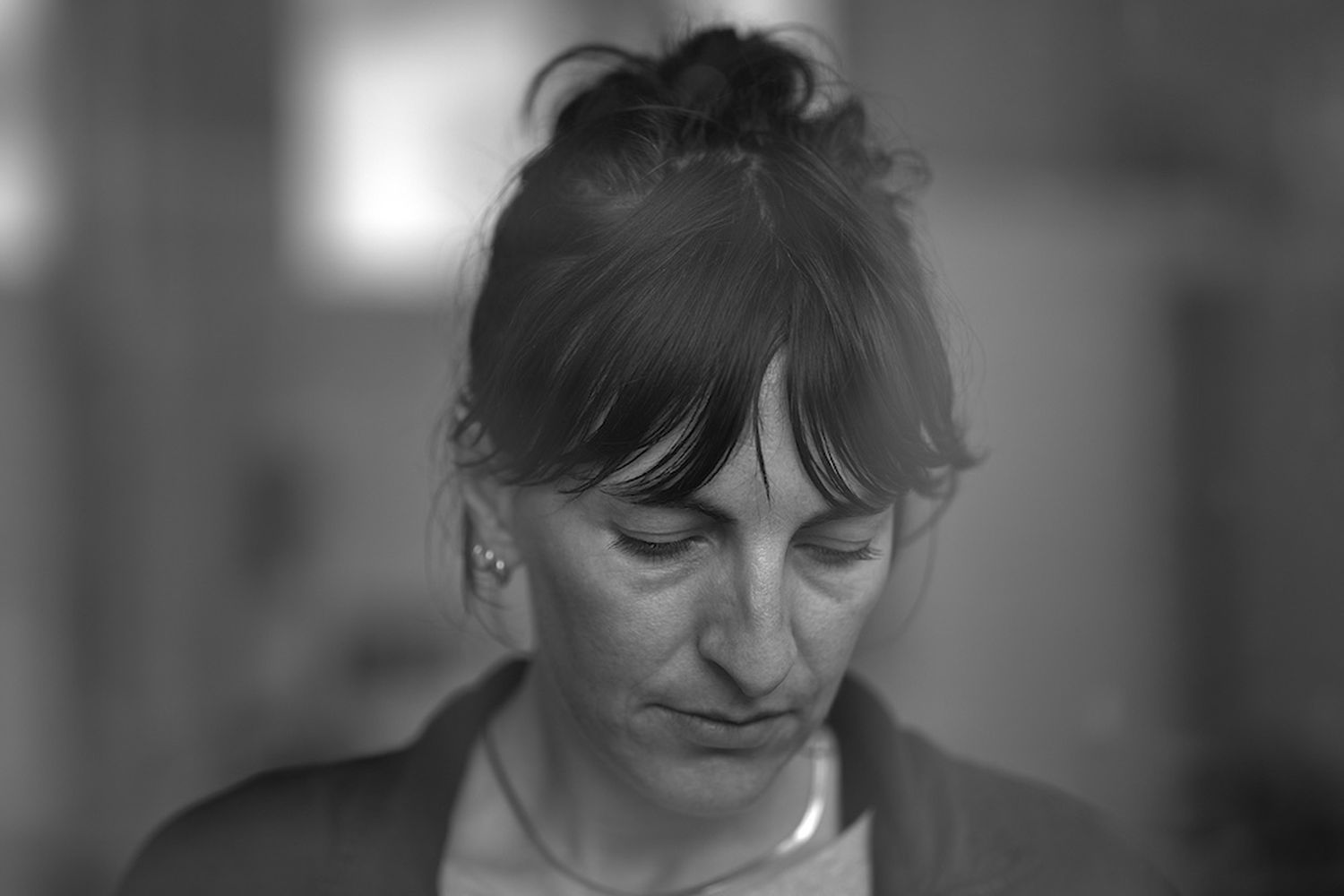 A woman with a bun in her hair, wearing a jacket and a necklace, is looking down at a cell phone. [G]