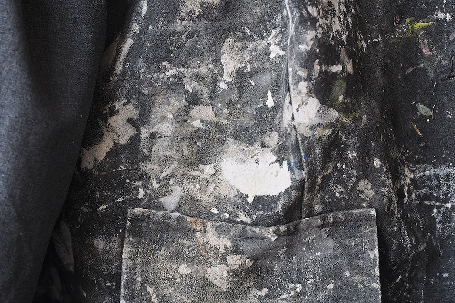 A close-up of a person's clothing, specifically a jacket, with a dirty and stained appearance. The jacket has a pocket and a collar, but the fabric appears to be stained with dirt and grime. [G]